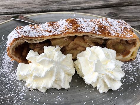 Una fetta di strudel di mele su un piatto, con panna montata accanto.