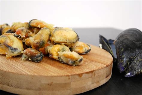 Un cestino pieno di cozze fritte dorate e croccanti, servite con spicchi di limone.