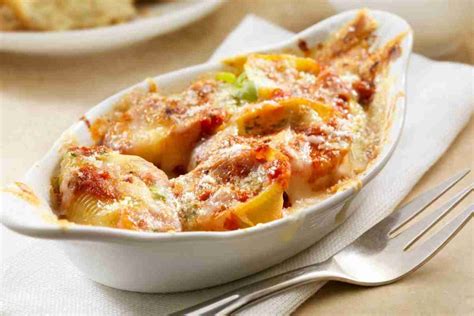 Descrizione: Un primo piano di conchiglioni ripieni al forno, dorati e filanti, pronti per essere serviti.
