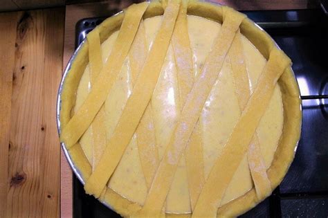 Immagine di una pastiera napoletana intera, decorata con strisce di pasta frolla a griglia, su un tavolo rustico.