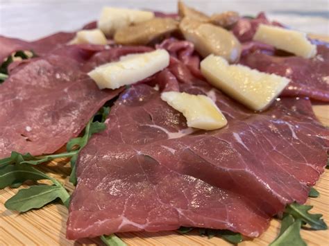 immagini di fette sottili di carne salada condita con olio e scaglie di grana