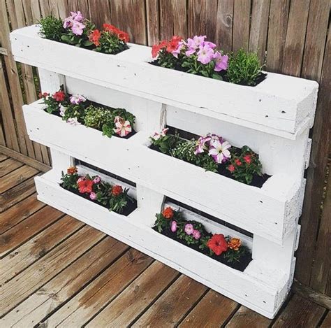 Pannello verticale realizzato con pallet e cassette di legno, adornato con vasi di fiori
