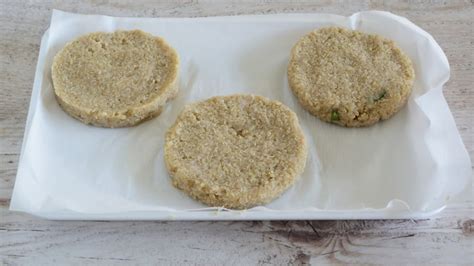 Immagine di burger di quinoa disposti su un vassoio con carta forno, pronti per essere congelati
