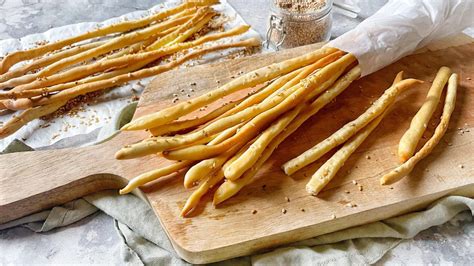 Immagine di grissini stirati dorati e croccanti su un tagliere di legno