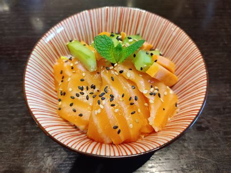 Fotografia appetitosa di un piatto di Chirashi Salmone e Avocado, con riso per sushi, fette di salmone rosa, avocado verde brillante e guarnizioni colorate come semi di sesamo e verdure.
