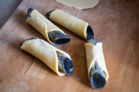 Primo piano della preparazione della scorza del cannolo: dischi di pasta arrotolati su cilindri metallici prima della frittura.
