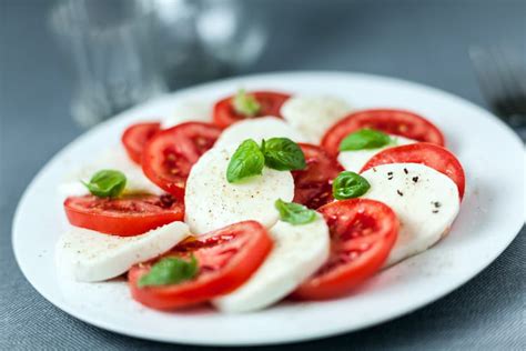 Une assiette colorée de Salade Caprese avec des tranches de tomates rouges, de mozzarella blanche et des feuilles de basilic vert frais.