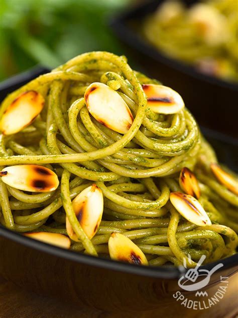 Immagine di un piatto di spaghetti al pesto di spinaci e mandorle con spinaci freschi e mandorle tostate.