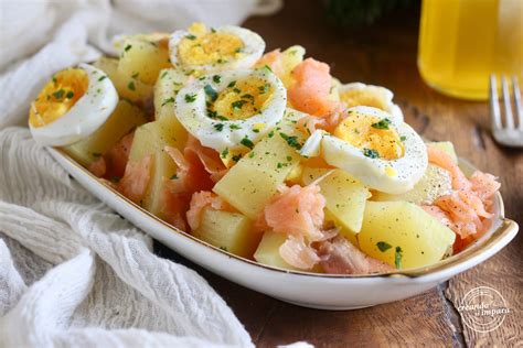 Un'insalata di patate, uova sode e salmone affumicato, condita con maionese e guarnita con erbe aromatiche.