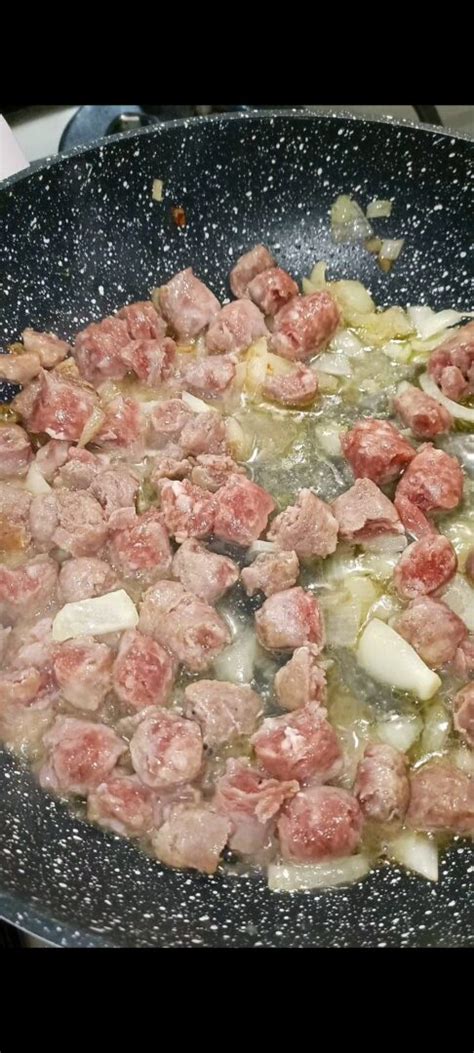 Primo piano di salsiccia rosolata in padella con cipolla e pancetta